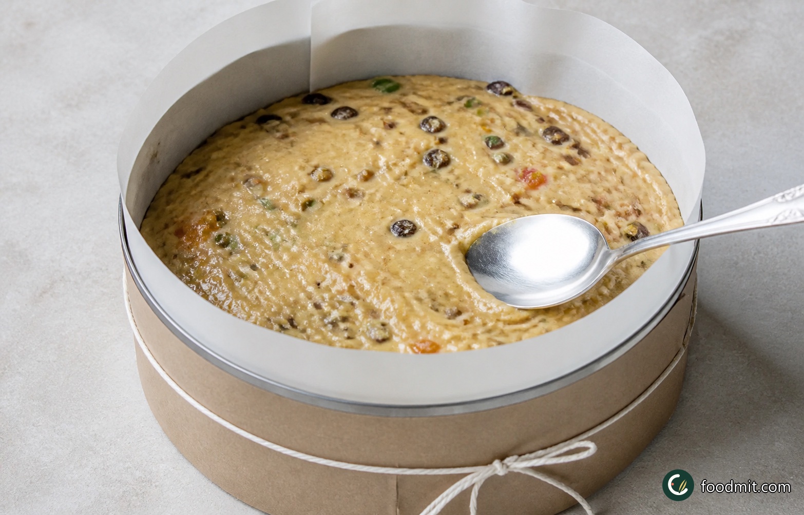 Spoon the heavy mixture into the prepared tin, working it gently into the edges so there are no obvious gaps. Level the surface with the back of the spoon. Tie a secure band of brown paper around the outside of the tin for insulation, then place the tin on an oven shelf positioned so the top of the cake sits approximately in the centre of the oven.