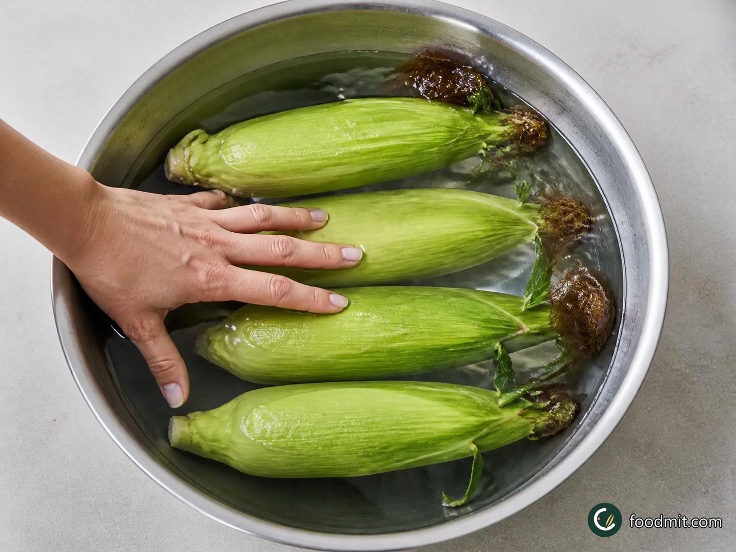 Submerge the corn, still enclosed in its husks, in cold water for at least 30 minutes. The soaked leaves will help shield the kernels from the fierce barbecue heat. If the only cobs available have already been husked, leave out the soaking step and proceed with them as they are.
